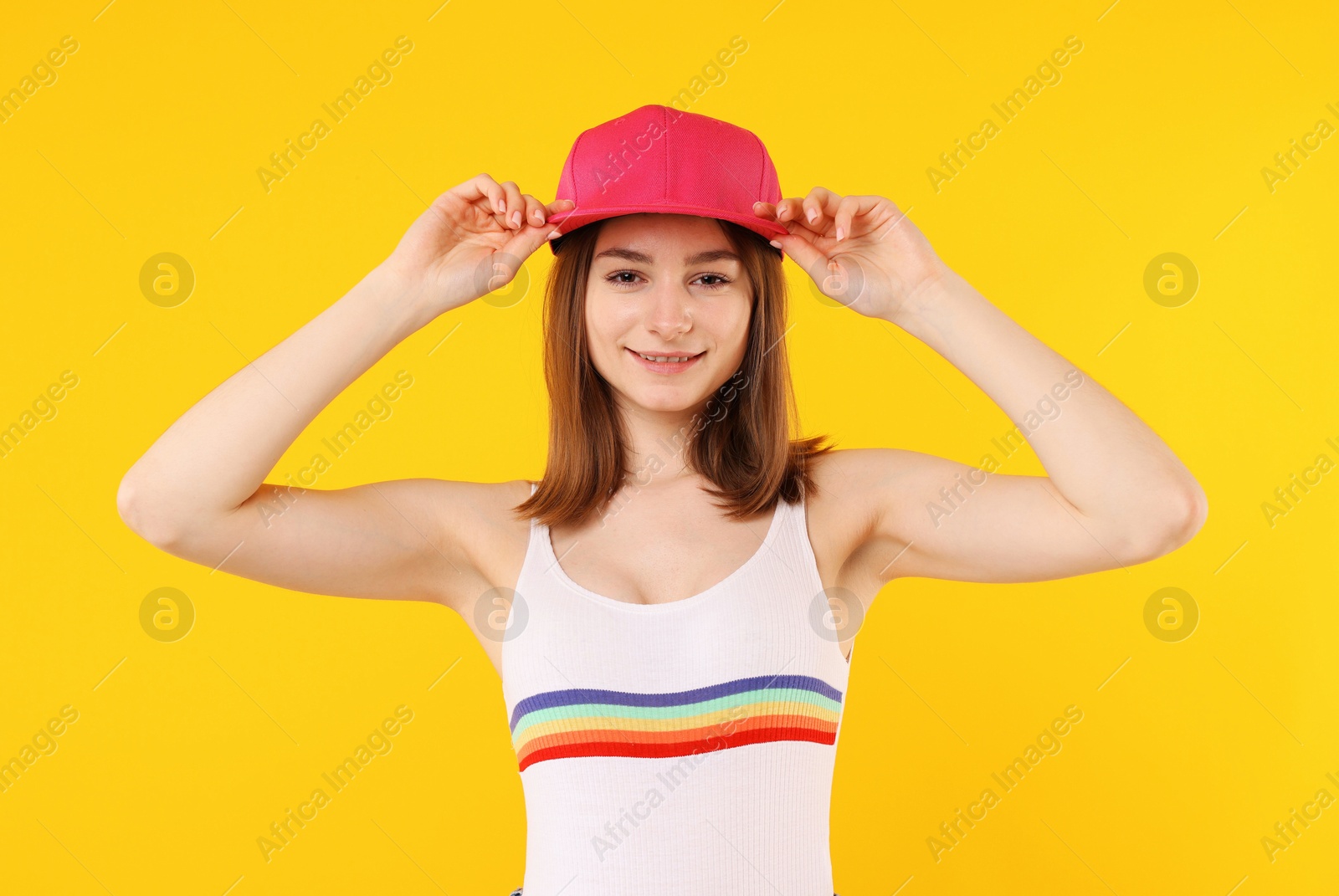 Young woman wearing stylish pink baseball hat on yellow background Photo of Young woman wearing stylish pink baseball hat on yellow background