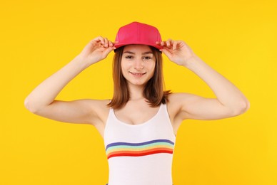 Photo of Young woman wearing stylish pink baseball hat on yellow background