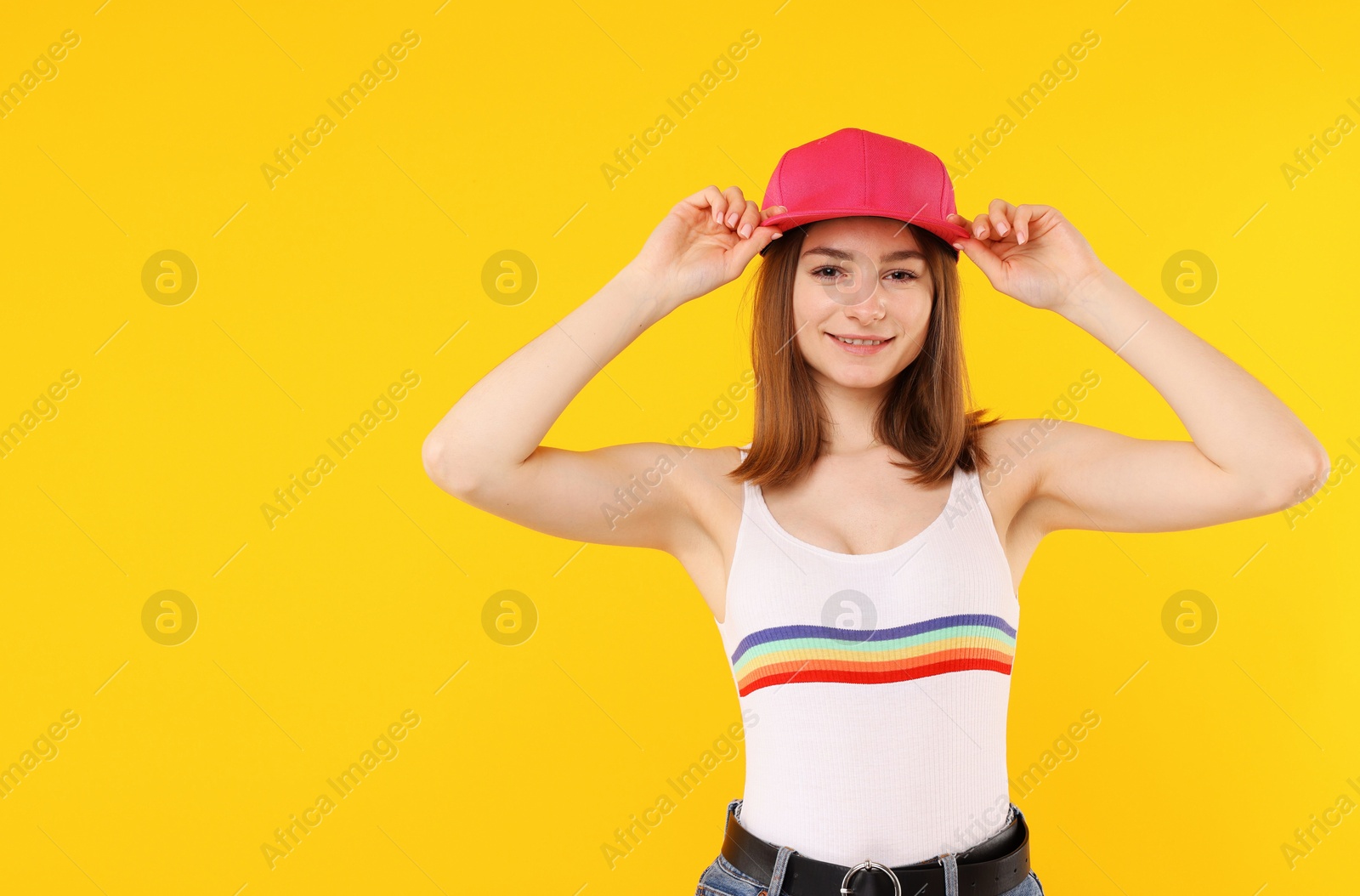 Young woman wearing stylish pink baseball hat on yellow background, space for text Photo of Young woman wearing stylish pink baseball hat on yellow background, space for text