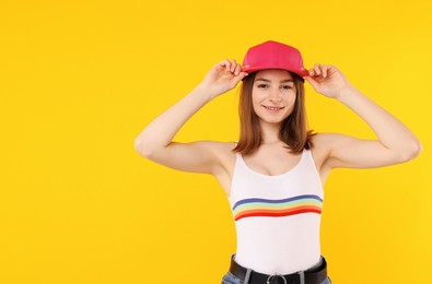 Photo of Young woman wearing stylish pink baseball hat on yellow background, space for text