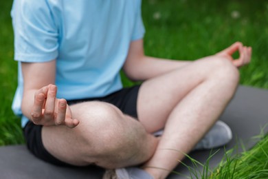 Photo of Young man practicing yoga on mat in park, closeup