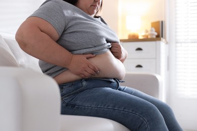 Photo of Woman with excessive belly fat on sofa indoors, closeup. Overweight problem