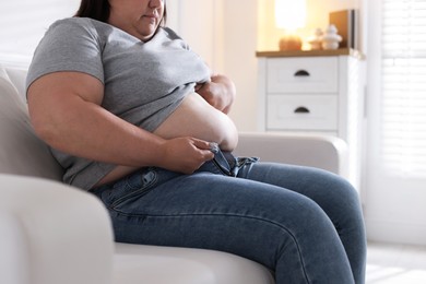 Photo of Overweight woman trying to put on tight jeans indoors, closeup