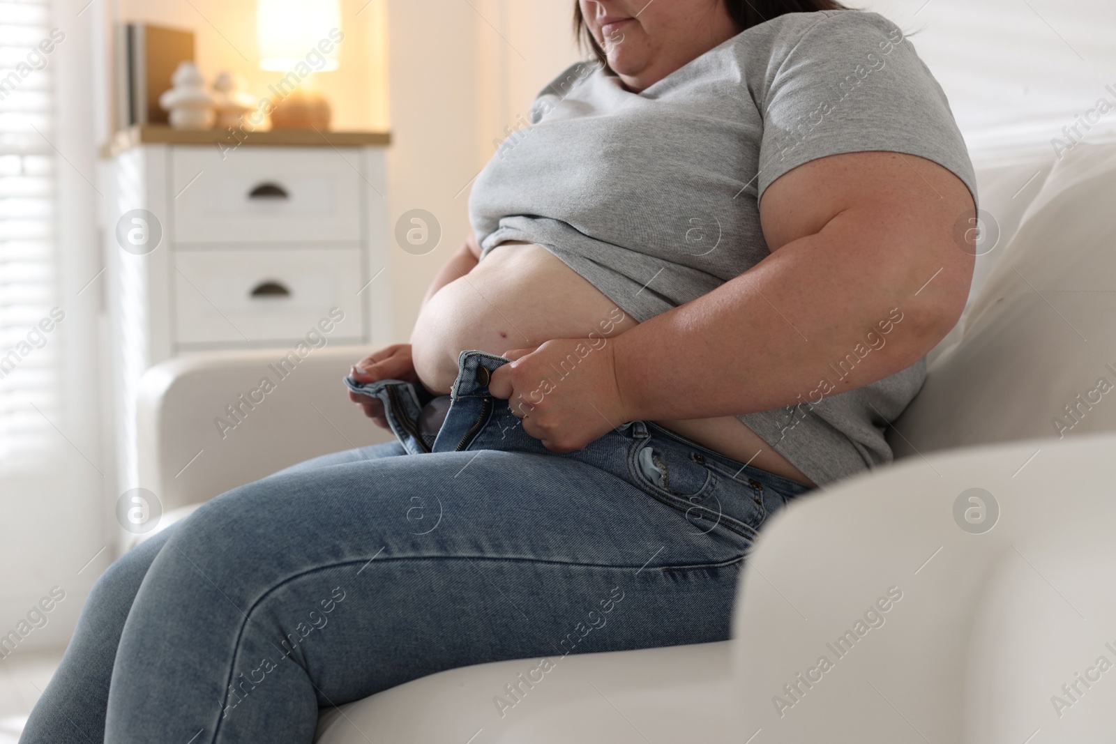 Overweight woman trying to put on tight jeans indoors, closeup Photo of Overweight woman trying to put on tight jeans indoors, closeup