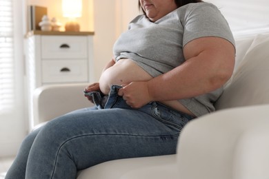 Photo of Overweight woman trying to put on tight jeans indoors, closeup