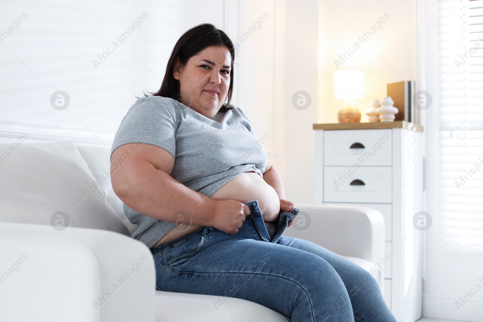 Overweight woman trying to put on tight jeans indoors Photo of Overweight woman trying to put on tight jeans indoors