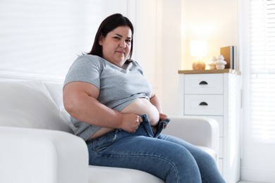 Photo of Overweight woman trying to put on tight jeans indoors