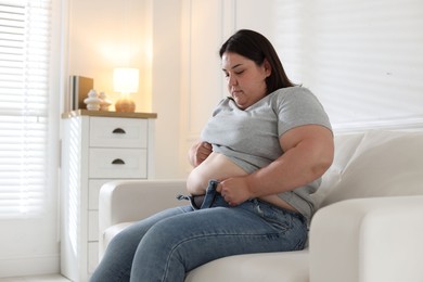 Photo of Overweight woman trying to put on tight jeans indoors