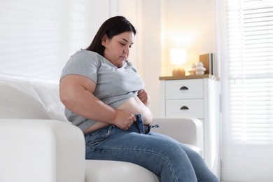 Photo of Overweight woman trying to put on tight jeans indoors