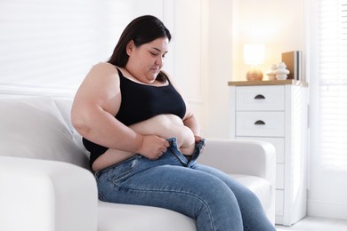 Photo of Overweight woman trying to put on tight jeans indoors