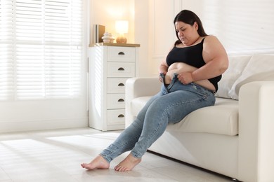 Photo of Overweight woman trying to put on tight jeans indoors, space for text