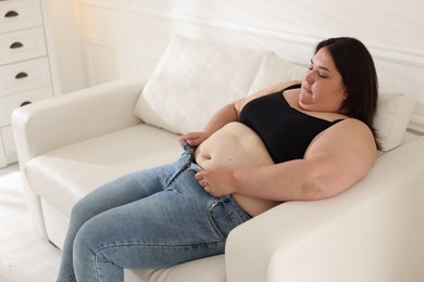 Photo of Overweight woman trying to put on tight jeans indoors