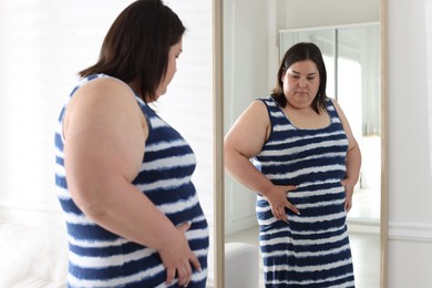 Photo of Overweight woman looking at herself in mirror indoors