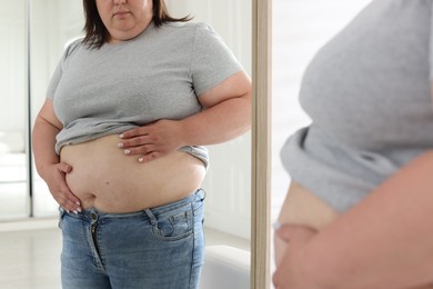 Photo of Woman with excessive belly fat near mirror indoors, closeup. Overweight problem