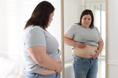 Photo of Woman with excessive belly fat near mirror indoors. Overweight problem