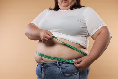 Photo of Overweight woman measuring her belly with tape on beige background, closeup