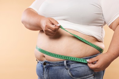 Photo of Overweight woman measuring her belly with tape on beige background, closeup