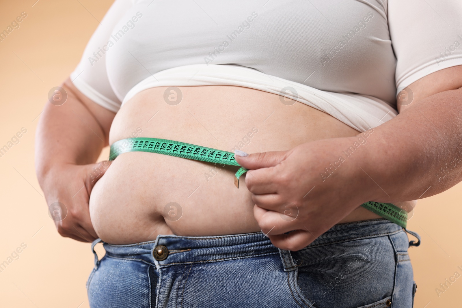 Overweight woman measuring her belly with tape on beige background, closeup Photo of Overweight woman measuring her belly with tape on beige background, closeup