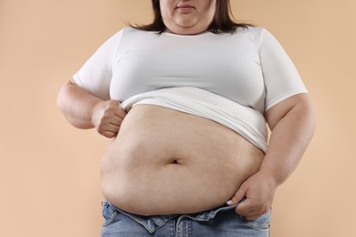 Photo of Woman with excessive belly fat on beige background, closeup