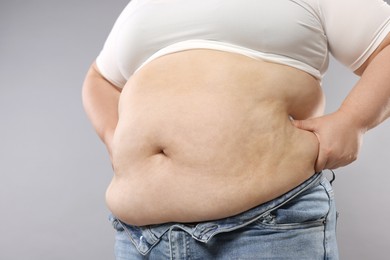 Photo of Woman with excessive belly fat on grey background, closeup. Overweight problem