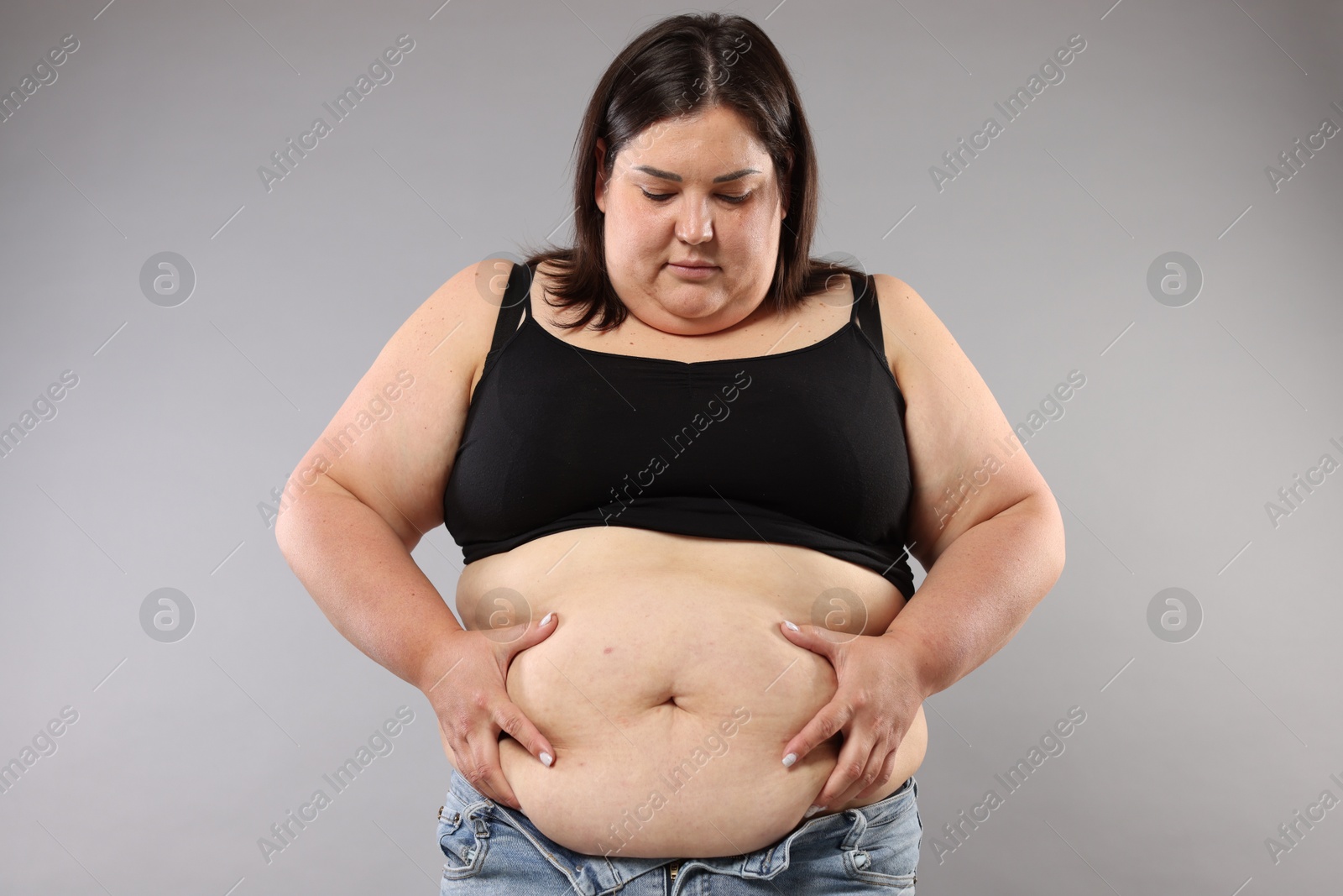 Woman with excessive belly fat on grey background. Overweight problem Photo of Woman with excessive belly fat on grey background. Overweight problem
