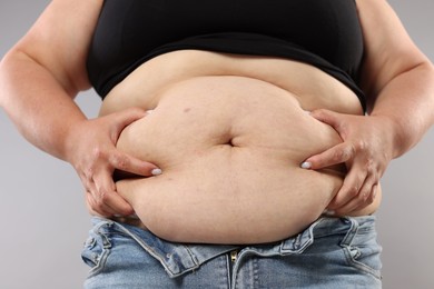 Photo of Woman with excessive belly fat on grey background, closeup. Overweight problem
