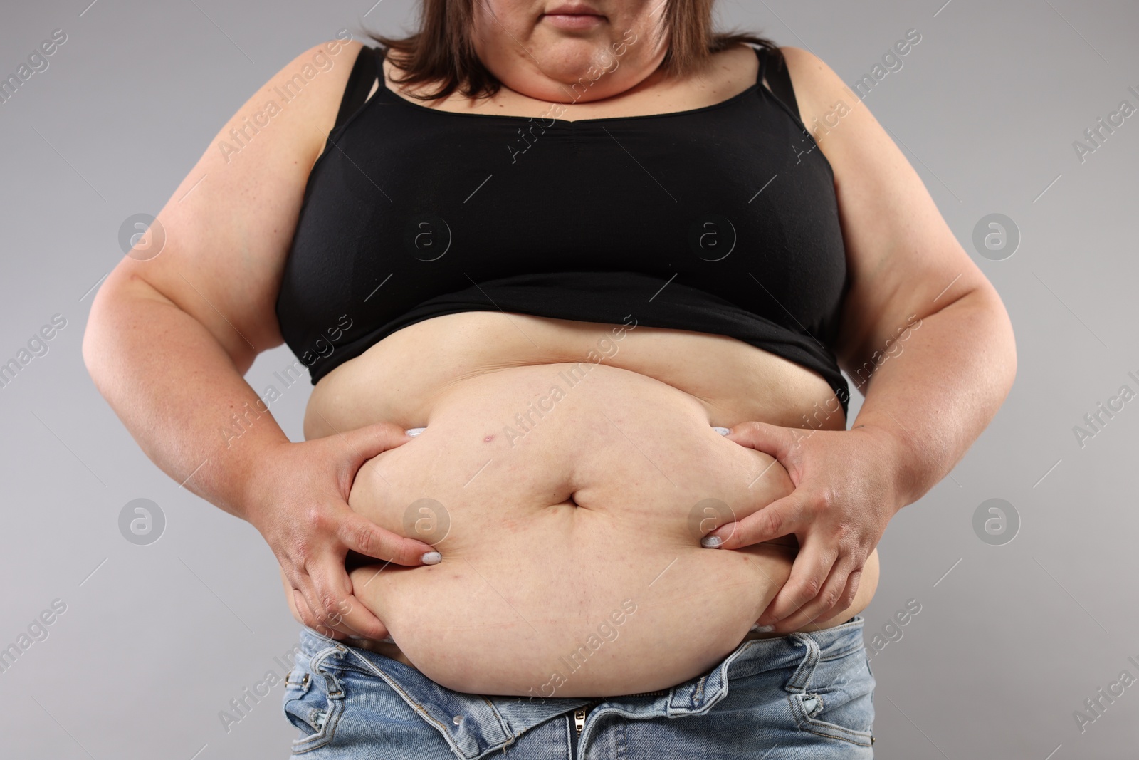 Woman with excessive belly fat on grey background, closeup. Overweight problem Photo of Woman with excessive belly fat on grey background, closeup. Overweight problem