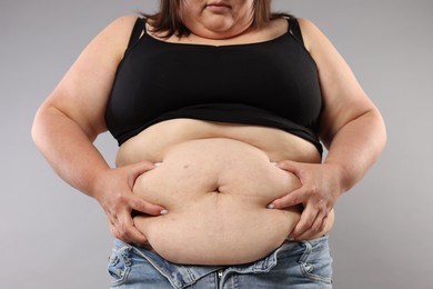 Photo of Woman with excessive belly fat on grey background, closeup. Overweight problem