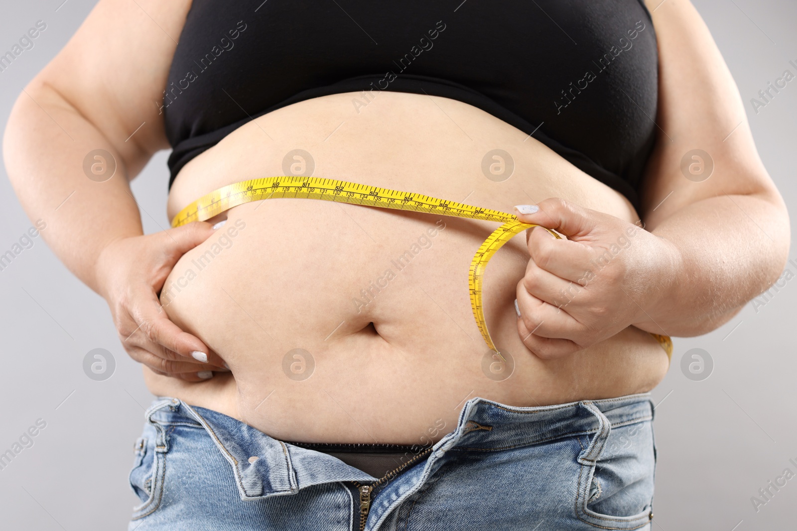 Overweight woman measuring her belly with tape on grey background, closeup Photo of Overweight woman measuring her belly with tape on grey background, closeup