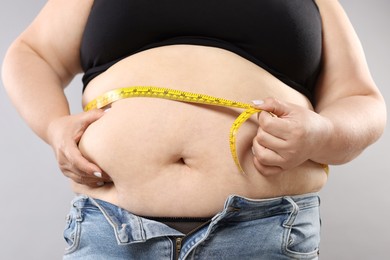 Photo of Overweight woman measuring her belly with tape on grey background, closeup