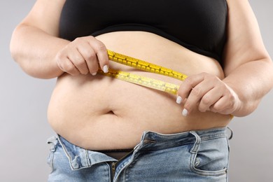 Photo of Overweight woman measuring her belly with tape on grey background, closeup
