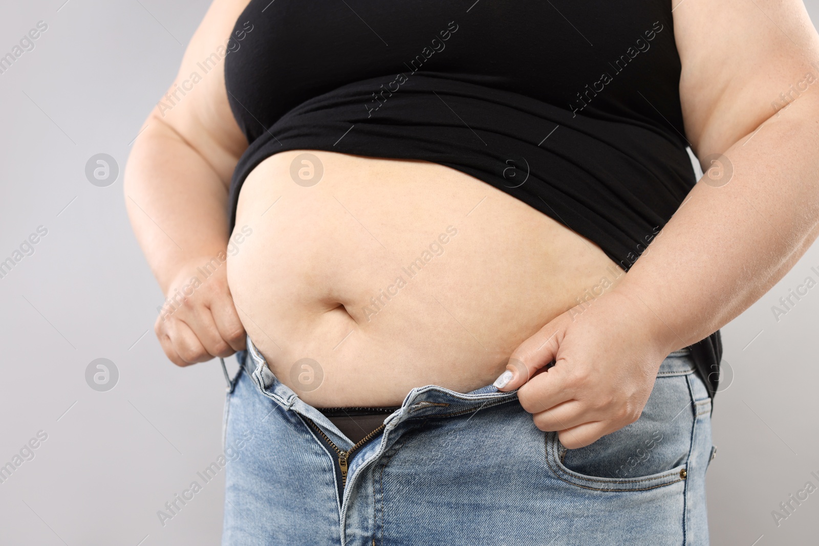 Overweight woman trying to put on tight jeans against grey background, closeup Photo of Overweight woman trying to put on tight jeans against grey background, closeup