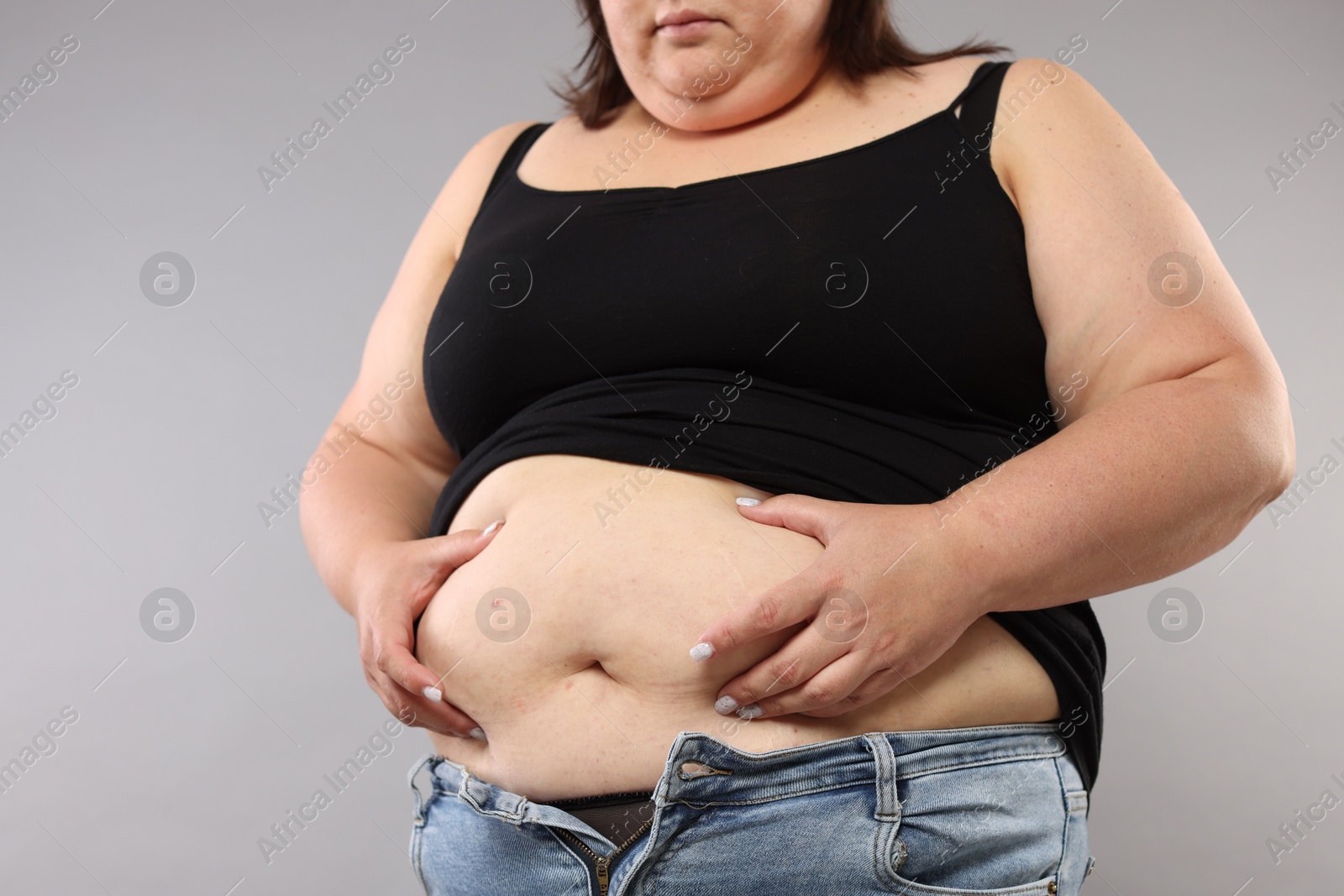 Woman with excessive belly fat on grey background, closeup Photo of Woman with excessive belly fat on grey background, closeup