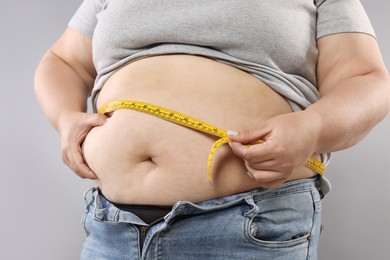 Photo of Overweight woman measuring her belly with tape on grey background, closeup