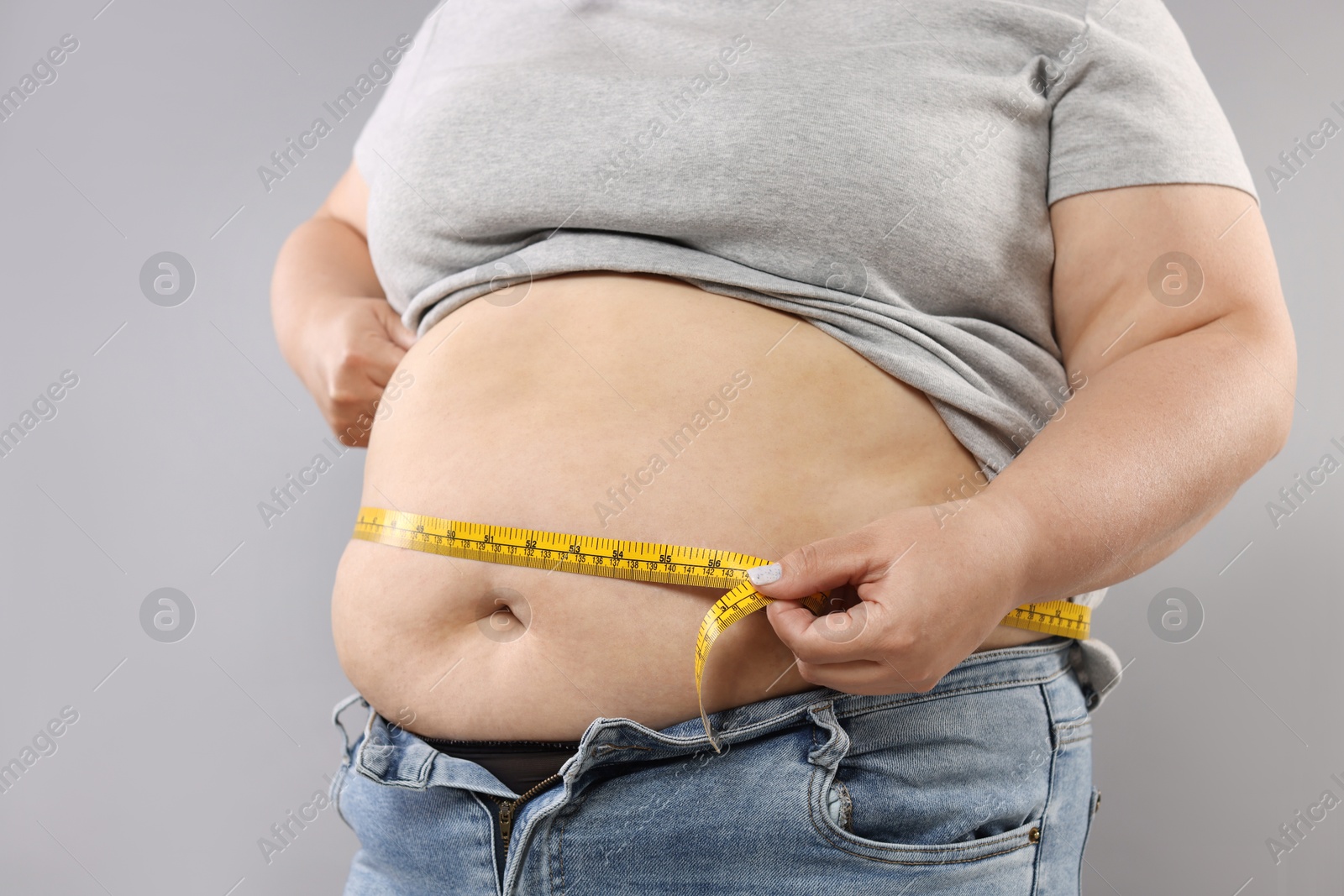 Overweight woman measuring her belly with tape on grey background, closeup Photo of Overweight woman measuring her belly with tape on grey background, closeup