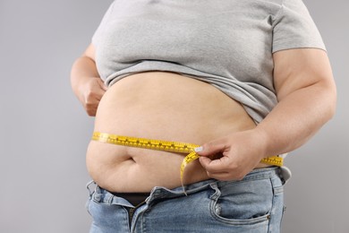Photo of Overweight woman measuring her belly with tape on grey background, closeup