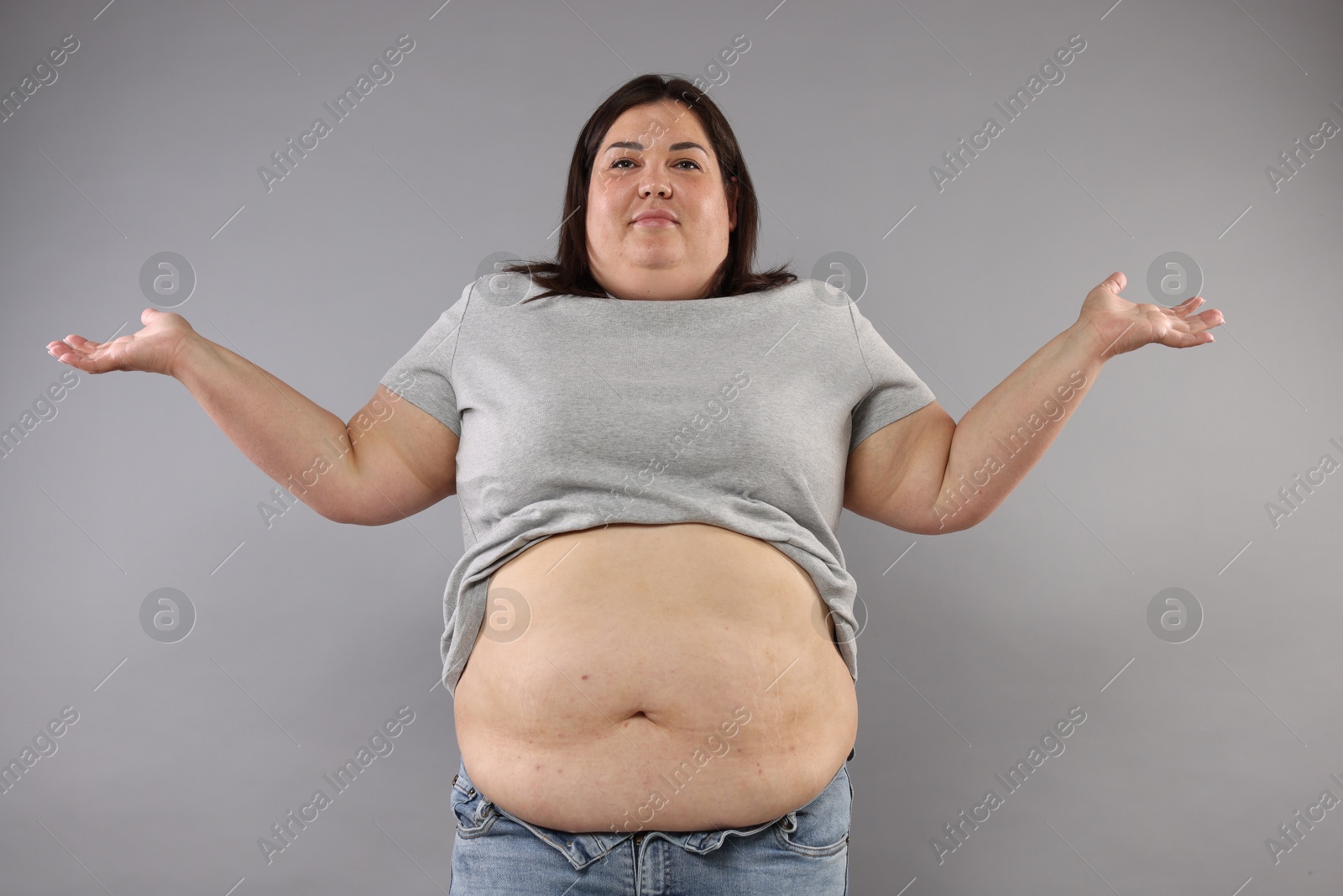 Woman with excessive belly fat on grey background Photo of Woman with excessive belly fat on grey background