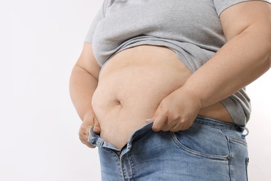 Photo of Overweight woman trying to put on tight jeans against white background, closeup. Space for text