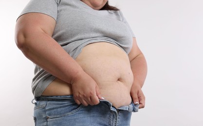 Photo of Overweight woman trying to put on tight jeans against white background, closeup. Space for text