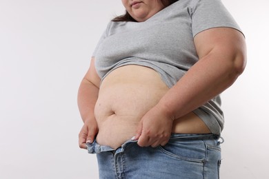 Photo of Overweight woman trying to put on tight jeans against white background, closeup. Space for text