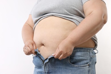 Photo of Overweight woman trying to put on tight jeans against white background, closeup