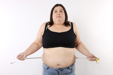 Photo of Overweight woman measuring her belly with tape on white background