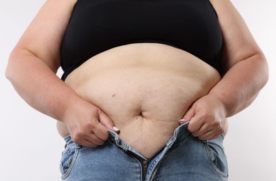 Photo of Overweight woman trying to put on tight jeans against white background, closeup