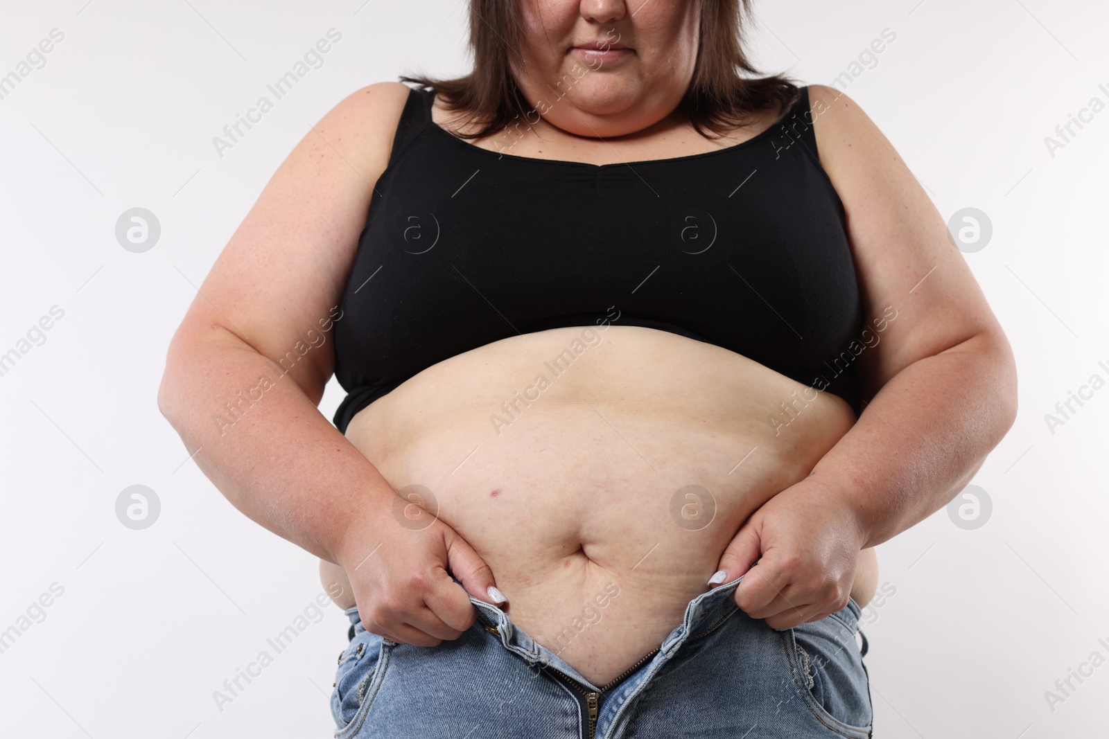 Photo of Overweight woman trying to put on tight jeans against white background, closeup
