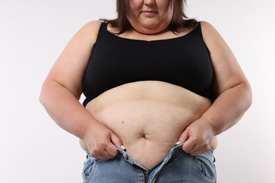 Photo of Overweight woman trying to put on tight jeans against white background, closeup