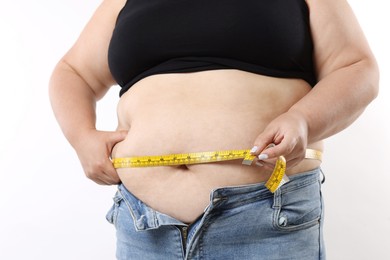 Photo of Overweight woman measuring her belly with tape on white background, closeup