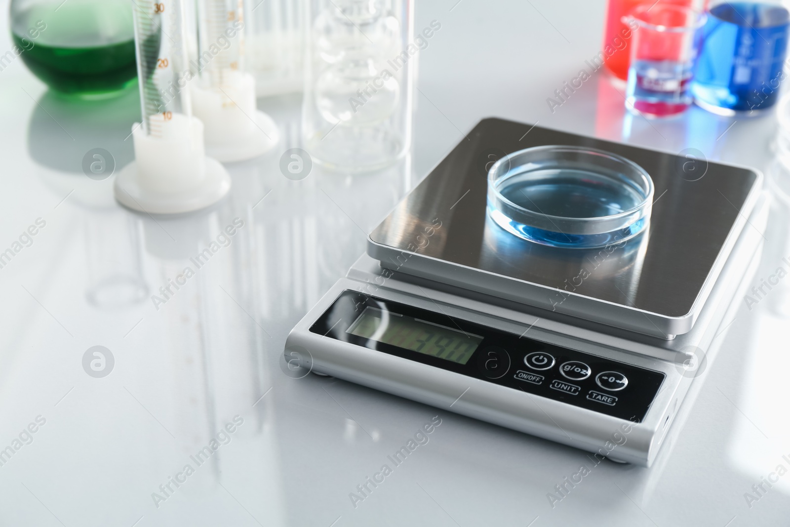 Scale with Petri dish of sample and other laboratory glassware on white mirror table, closeup Photo of Scale with Petri dish of sample and other laboratory glassware on white mirror table, closeup