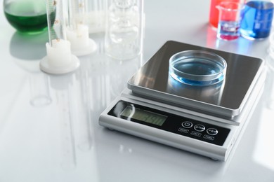 Photo of Scale with Petri dish of sample and other laboratory glassware on white mirror table, closeup