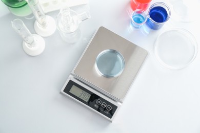 Photo of Scale with Petri dish of sample and other laboratory glassware on white table, flat lay