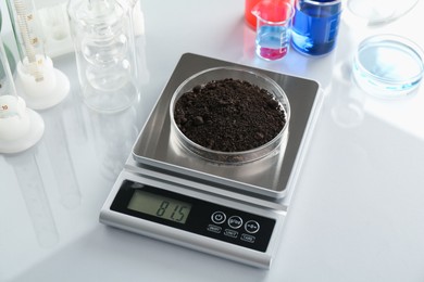 Photo of Scale with Petri dish of sample and other laboratory glassware on white mirror table, closeup
